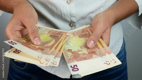 Counting 50 euro bills in hands. A woman in a white shirt counts money.