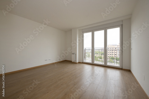 Empty room with light wooden floors and a balcony with three aluminum and glass doors with views