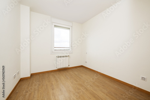 Empty room with light wooden floors, white aluminum radiators, smooth white painted walls and a white aluminum and glass single pane window