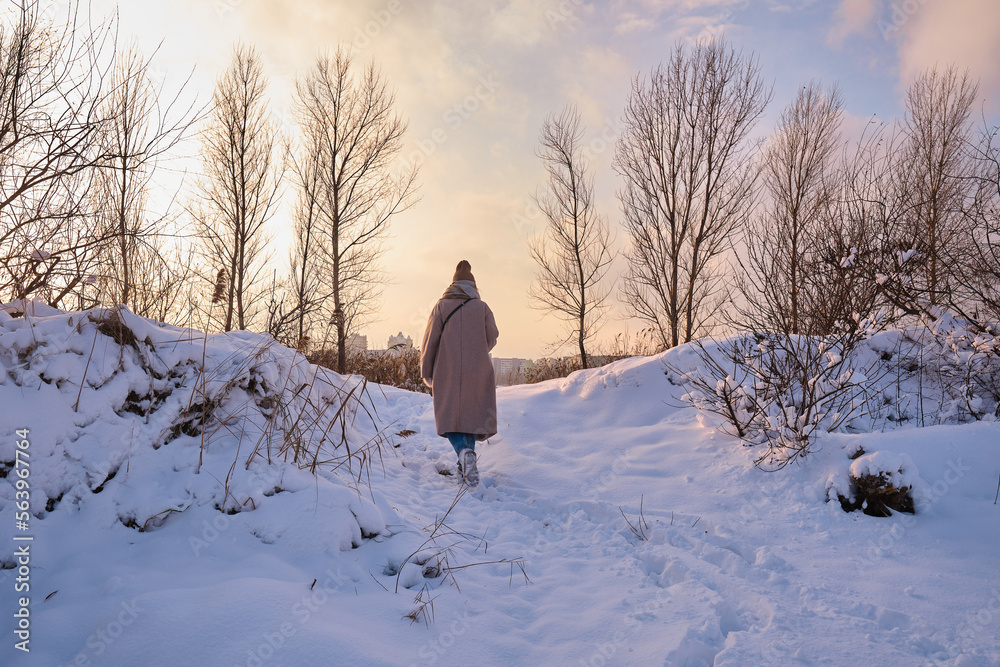Fototapeta premium A young woman walks in the snow on a sunny frosty day, enjoying winter moments and nature, wearing winter clothes. Winter time concept, walk
