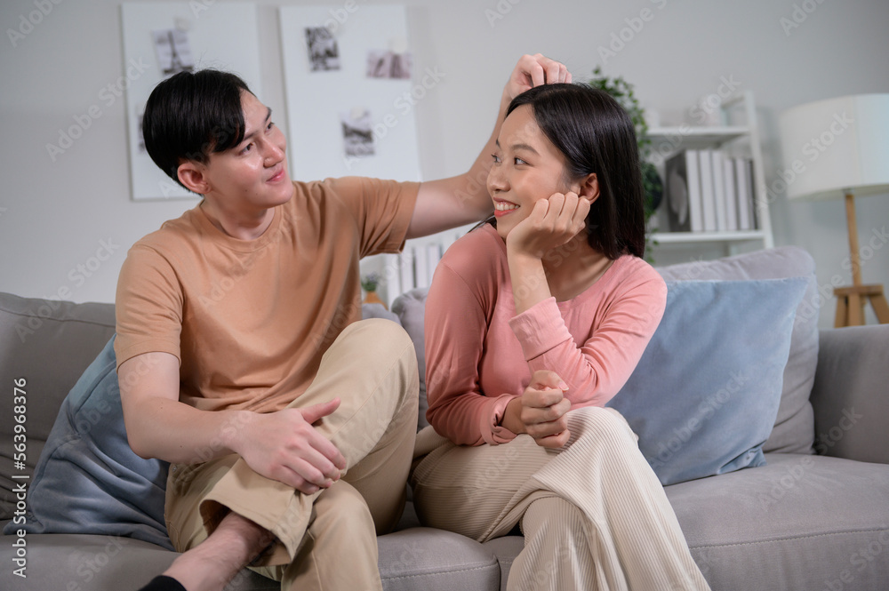 Happy young Asian couple sitting on sofa relaxing together in living room at home Happy young Asian couple sitting on sofa relaxing together in living room at home