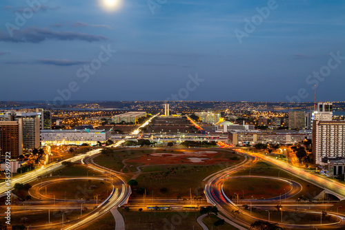 Brasilia city in a colorful long exposure shot during night. Aerial view of the city structure. The congress and ministries are visible far away. Full moon above the sky.