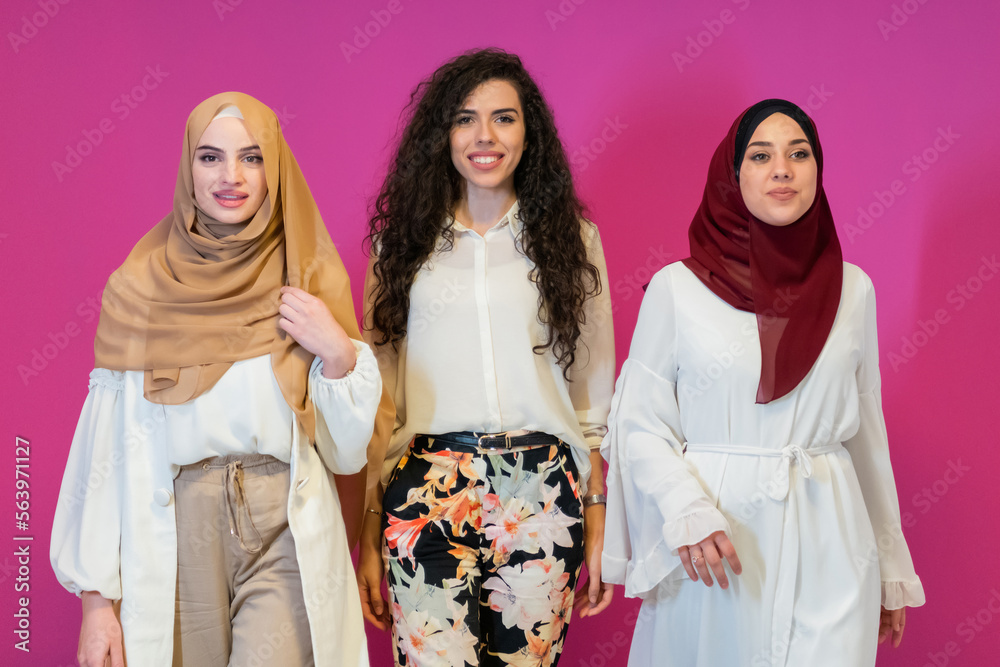 Group portrait of beautiful muslim women two of them in fashionable dress with hijab isolated on pink background representing modern islam fashion and ramadan kareem concept