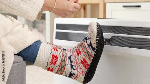 Closeup of woman feeling cold at home warming at electric heater. Concept of energy crisis, high bills, economy and saving money on monthly utility payments