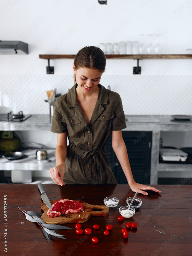 A woman smiling with teeth prepares dinner in the kitchen of fresh organic and organic products wooden table against the backdrop of a stylish kitchen interior in the style of elevator and minimalism.