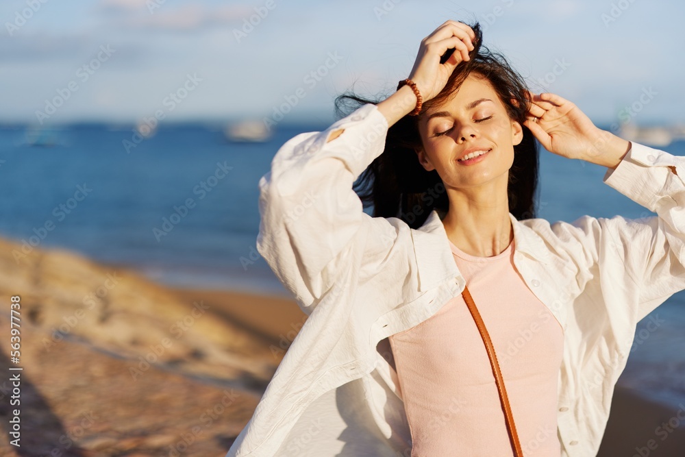 A woman with her eyes closed in the sun against the ocean smile with teeth, flying hair, tanned skin, rest, the concept of skin care in summer and spring.