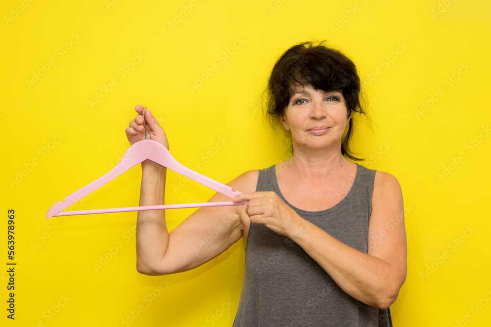 beautiful senior woman holding empty pink hanger on yellow background beautiful senior woman holding empty pink hanger on yellow background