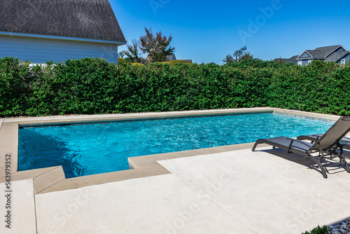 Fototapeta A rectangular new swimming pool with tan concrete edges in the fenced backyard o
