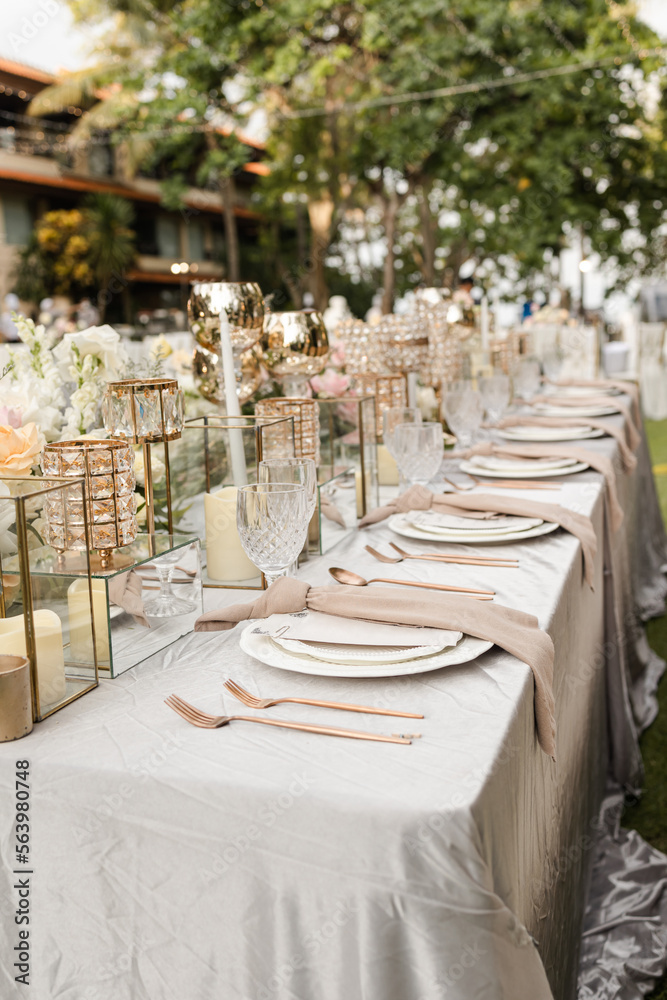 Beautiful outdoor wedding decoration in garden. Long table decorated with flowers, candles and accessories. Open air wedding banquet on green lawn
