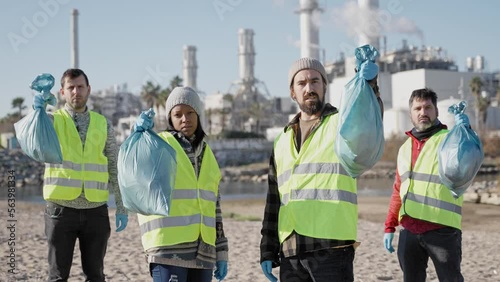 Team of activists cleaning plastic rubish waste in industrial river sea shore near factory photo