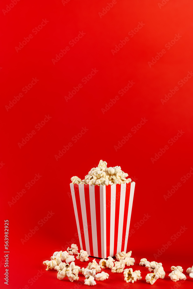 Popcorn in a red and white striped bag on a red background. Front view, copy space