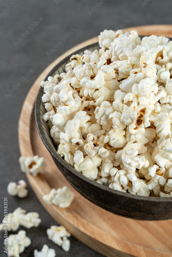 popcorn in a bowl on a wooden board and gray concrete background, closeup and selected focus popcorn in a bowl on a wooden board and gray concrete background, closeup and selected focus