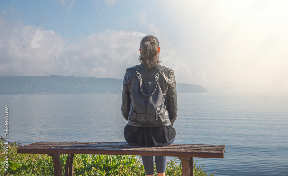 Woman sitting on the bench near the sea or lake.