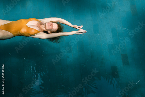A beautiful girl in a yellow swimsuit swims on her back in the pool, top view.