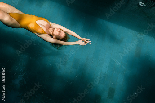 A beautiful girl in a yellow swimsuit swims on her back in the pool, top view.