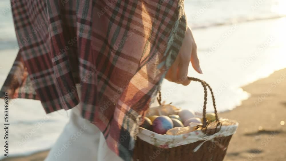 A girl walks along the beach at sunset carrying a basket of Easter eggs. I'm walking towards the sun, the sea waves are behind me. A girl walks along the beach at sunset carrying a basket of Easter eggs. I'm walking towards the sun, the sea waves are behind me.