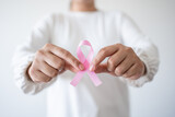 Woman holding pink ribbon as symbol of World Cancer day, breast cancer awareness sign