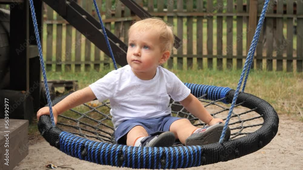 Happy smiling baby boy swinging in rope nest swing on playground. Kids playing outdoors, children having fun, summer vacation. Happy smiling baby boy swinging in rope nest swing on playground. Kids playing outdoors, children having fun, summer vacation.