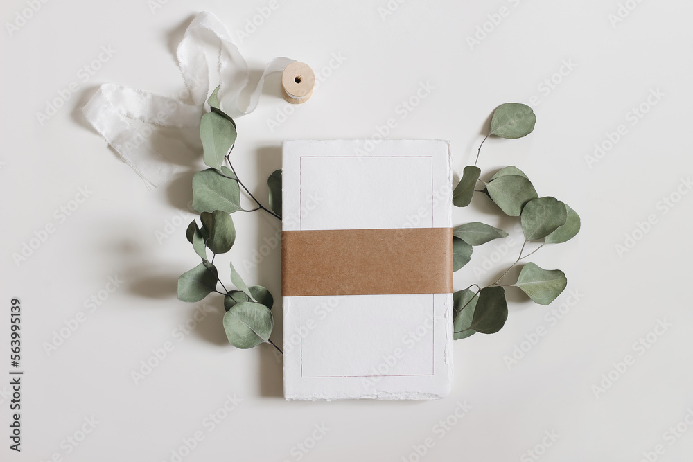 Blank notepad mockup. Cotton paper diary with rough edges, craft belly band, tape isolated on white table background. Dry eucalyptus leaves, branch. Wedding composition, office supply. Flatlay, top. - obrazy, fototapety, plakaty 