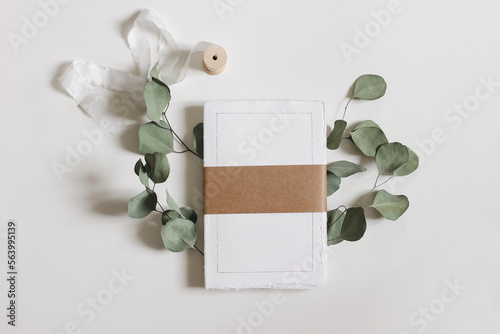 Blank notepad mockup. Cotton paper diary with rough edges, craft belly band, tape isolated on white table background. Dry eucalyptus leaves, branch. Wedding composition, office supply. Flatlay, top.