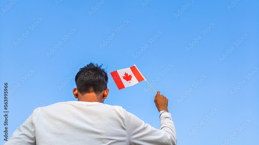 Boy holding Canada flag against clear blue sky. Man hand waving Canadian flag view from back, copy space Boy holding Canada flag against clear blue sky. Man hand waving Canadian flag view from back, copy space