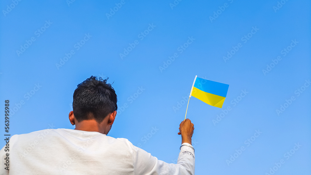 Boy holding Ukraine flag against clear blue sky. Man hand waving Ukrainian flag view from back, copy space Boy holding Ukraine flag against clear blue sky. Man hand waving Ukrainian flag view from back, copy space