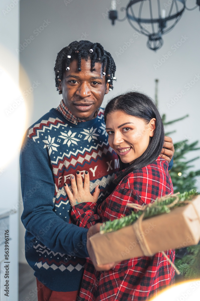 Diverse young couple hugging with presents near the Christmas tree. High quality photo