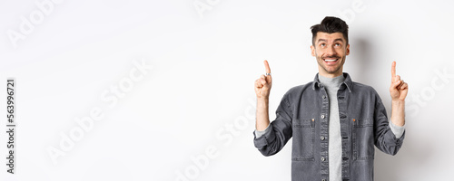 Cheerful caucaisan man with moustache pointing and looking up, smiling dreamy, showing cool promotion deal, standing on white background photo