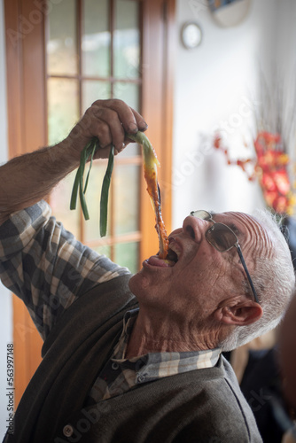 Older man inside a house eating a calçot. Tender onion with typical winter sauce in Catalonia. photo