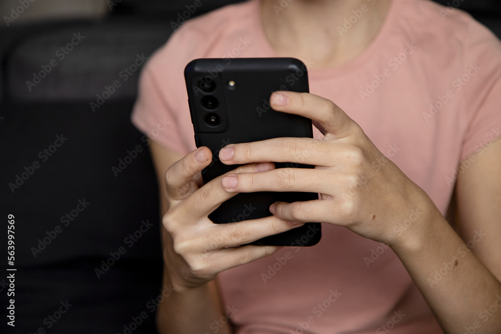 Teenage girl using smartphone, presses her finger, reads social networks on the Internet, types text or makes in-app purchases, mobile phone in two hands. Teenage girl using smartphone, presses her finger, reads social networks on the Internet, types text or makes in-app purchases, mobile phone in two hands.