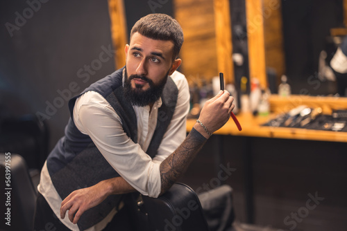 Dark-haired bearded man in a stylish outfit at the barbershop