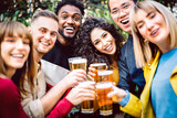 Front view of friends drinking and toasting beer at brewery bar restaurant patio - Happy hour promotion concept with people having fun together inviting guest at brew outdoor pub - Bright vivid filter
