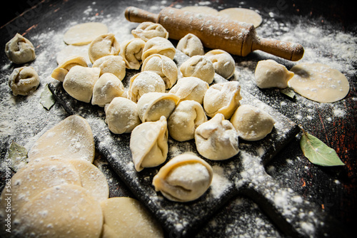 Raw homemade dumplings on a cutting board with a rolling pin. © Artem Shadrin