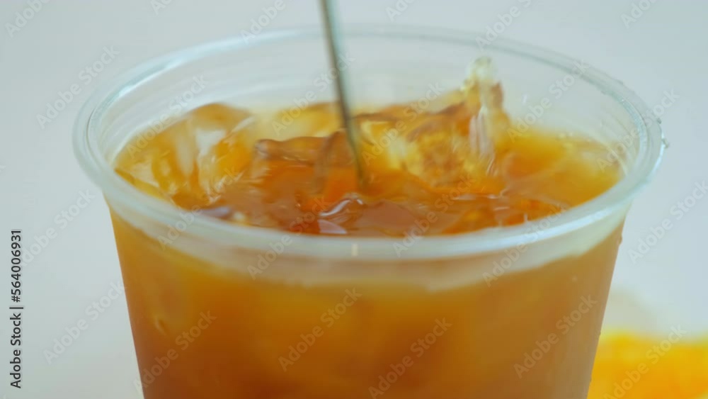 a hand is stirring ice in a cold hornet with a spoon. a hand stirs ice in cold orange coffee with a spoon. orange juice with ice a hand is stirring ice in a cold hornet with a spoon. a hand stirs ice in cold orange coffee with a spoon. orange juice with ice