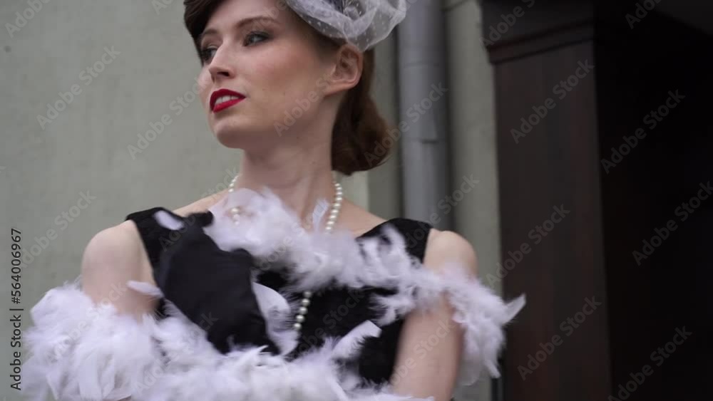 A woman stands in a white feather boa on the porch against a light wall. Slow motion of a woman in a historical costume of the 20-30s of the XX century. High quality FullHD footage A woman stands in a white feather boa on the porch against a light wall. Slow motion of a woman in a historical costume of the 20-30s of the XX century. High quality FullHD footage