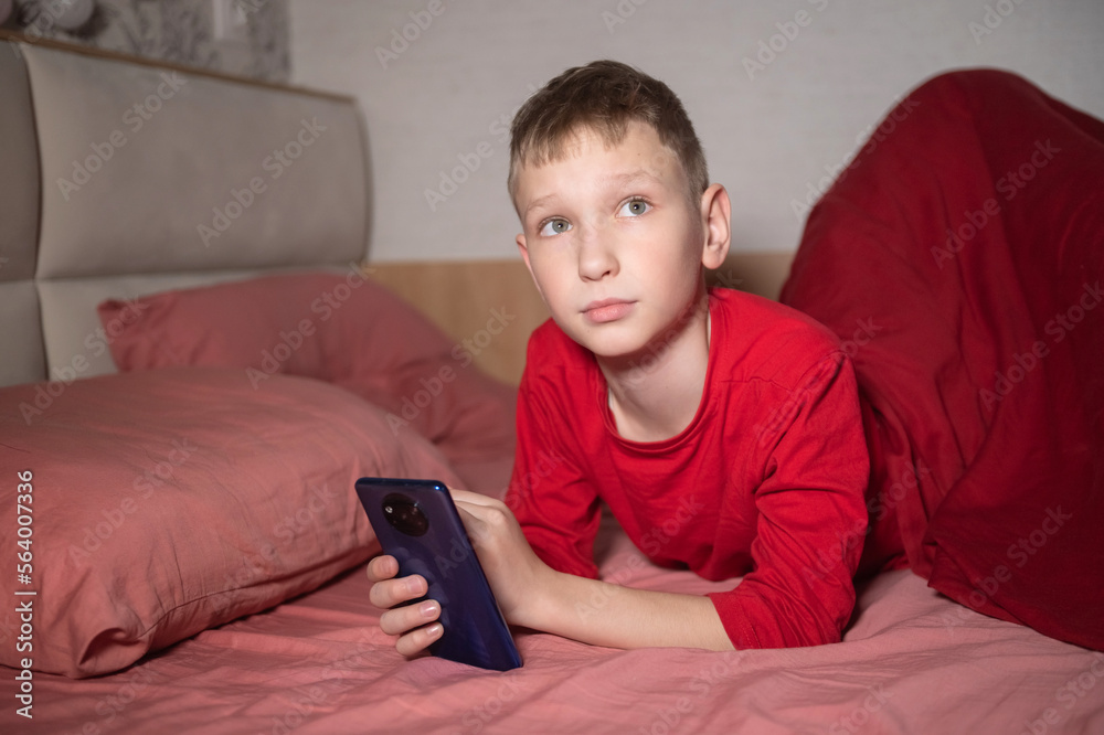 A cute boy in red pajamas is lying in bed and holding a phone A cute boy in red pajamas is lying in bed and holding a phone