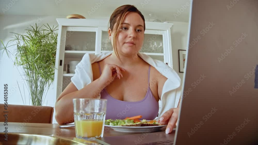 Happy plus size woman watching something at the laptop in cook room during the breakfast Happy plus size woman watching something at the laptop in cook room during the breakfast