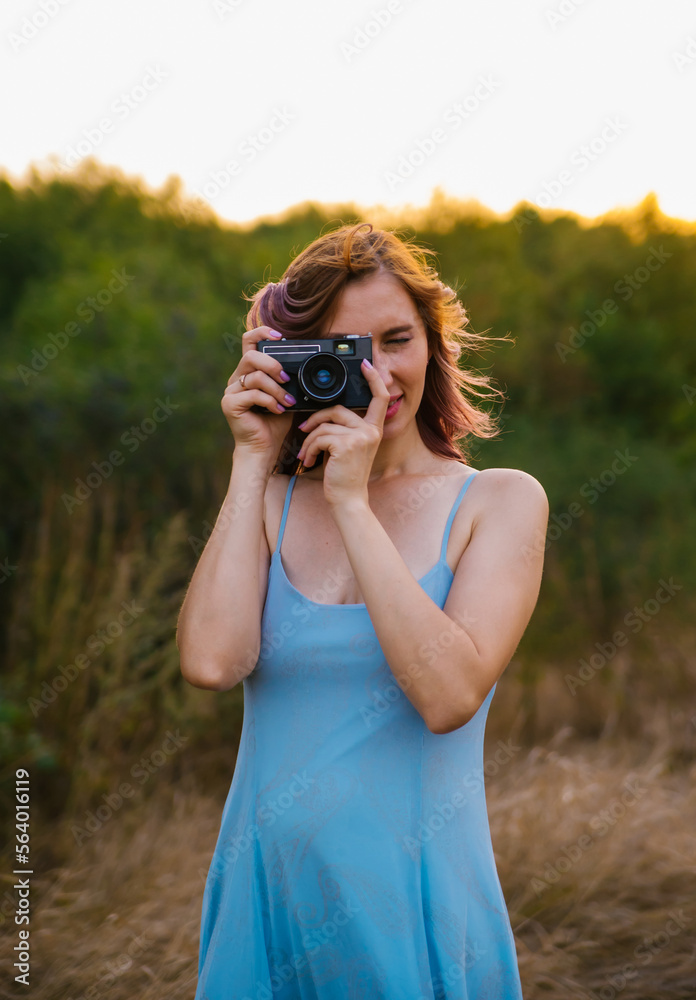 A young woman walks through a clearing with a camera. Hobbies and work. A walk in the park or forest. Outdoor recreation. The atmosphere of freedom and nature. A young woman walks through a clearing with a camera. Hobbies and work. A walk in the park or forest. Outdoor recreation. The atmosphere of freedom and nature.