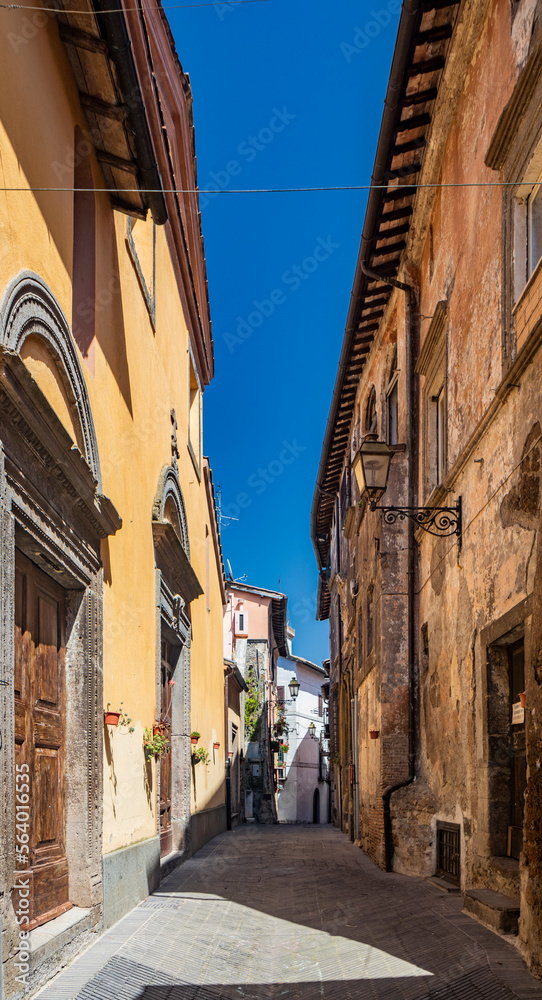 The small medieval village of Corchiano, in the province of Viterbo, in Lazio. The narrow streets of the small town with the old brick houses. The blue sky on a sunny day in summer.