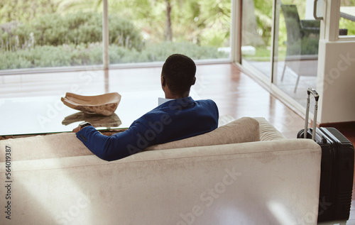 Thinking, immigration and vision of businessman on a couch or sofa in a hotel sitting looking at a window. Rear view, travel and back of professional corporate worker waiting in lounge or living room