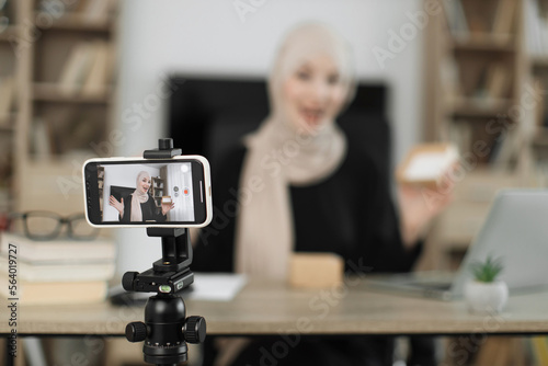 Focus on phone of attractive muslim female blogger unpacking gift boxes presents from companies and doing live streaming. Arab woman using smart phone camera for creating content.