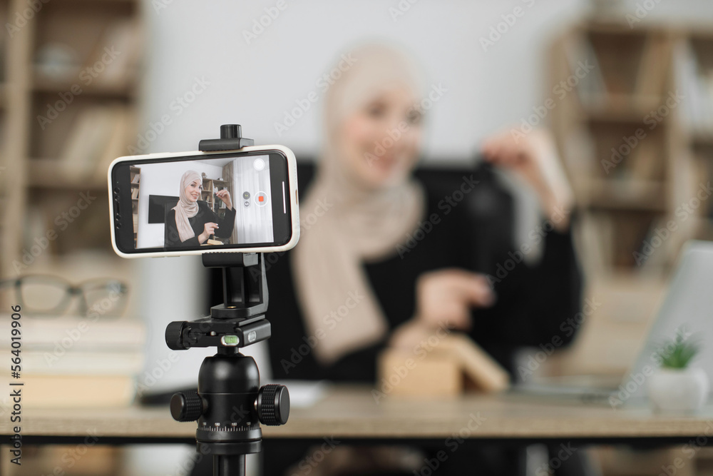 Focus on smart phone screen, muslim woman doing live stream while unpacking box with new smart watch. Female blogger sharing her feedback about modern gadget with her subscribers. Focus on smart phone screen, muslim woman doing live stream while unpacking box with new smart watch. Female blogger sharing her feedback about modern gadget with her subscribers.