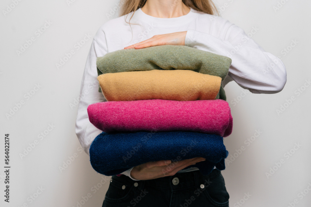 A young woman holds four warm sweaters in her hands on a white isolated background. Concept of winter wardrobe, dry cleaning of woolen clothes A young woman holds four warm sweaters in her hands on a white isolated background. Concept of winter wardrobe, dry cleaning of woolen clothes