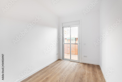 Bright room with white walls, light brown wooden parquet. The room has sliding glass doors in a metal frame with access to a balcony and a view of the neighboring house. Room for living.