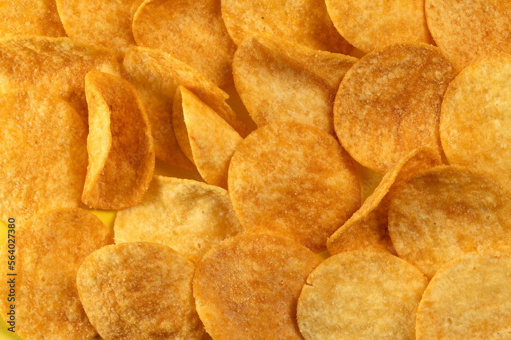 Potato chips scattered on the table close-up on a yellow background. Food with elevated cholesterol levels Potato chips scattered on the table close-up on a yellow background. Food with elevated cholesterol levels