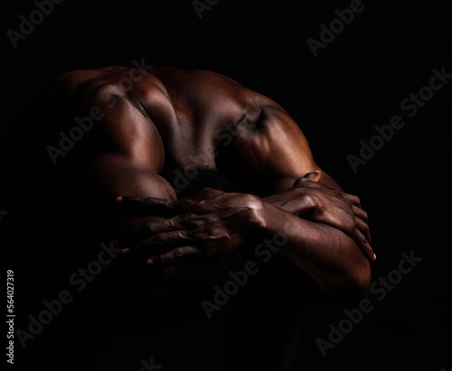 Art, masculinity and artistic shadows with african man posing naked in studio isolated against a dark background. Muscular, macho and artwork of a strong black man curled up with hands over his head