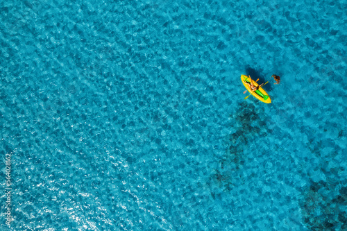 Summer sea vacation concept. Aerial view of yellow kayak in blue sea in summer. Sup board top view from drone. Woman relaxing on floating canoes in clear water