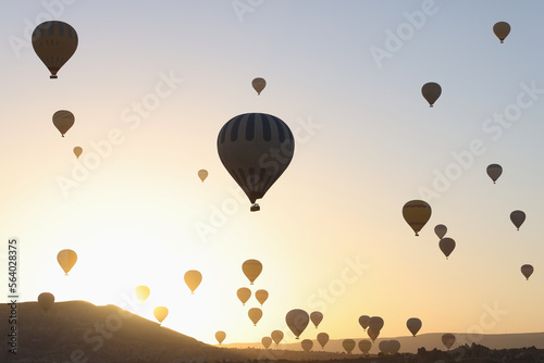 Sunset sky and many hot air balloons over hills.