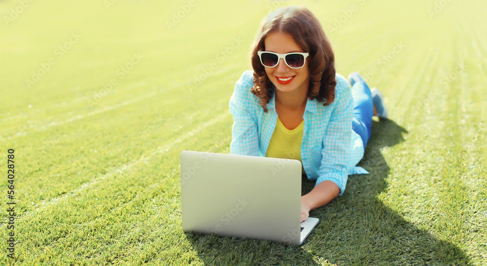 Young woman with laptop in the park on green grass background Young woman with laptop in the park on green grass background