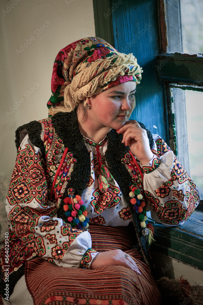 Ukrainian hutsul woman in national costume sitting by the window. 